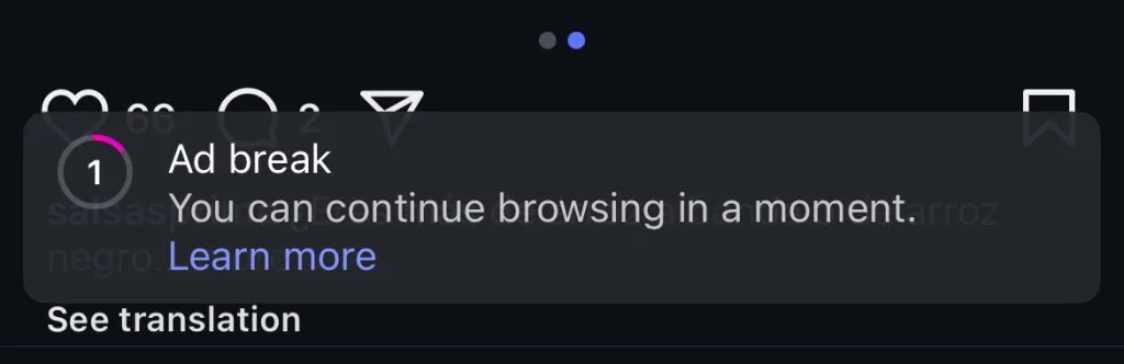 Screenshot of an Instagram screen showing a message overlay that reads: “Ad break. You can continue browsing in a moment.” There's a purple "Learn more" link and a "See translation" option below the message. In the background, blurred Instagram interface elements are visible, including likes, comments, and the message icon.
